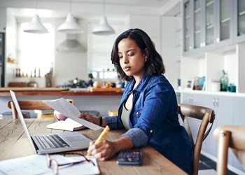 Woman manages finances at home with laptop.