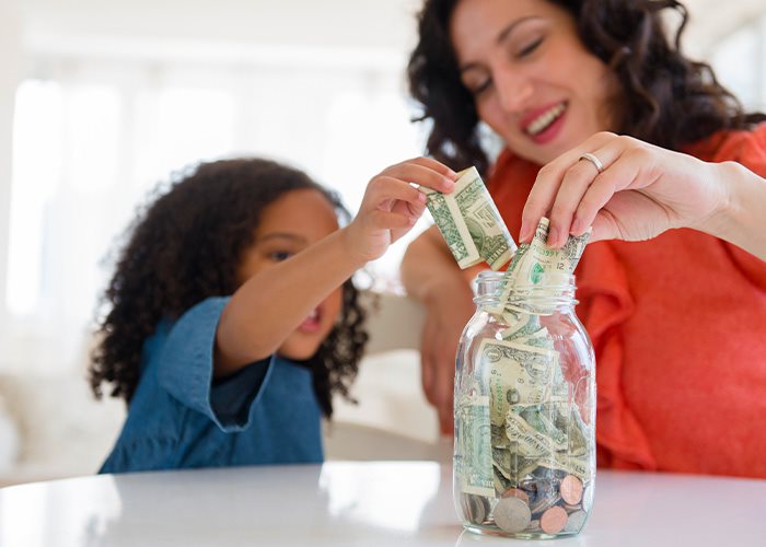 A parent teaches their child the basics of saving and money by filling a jar with saved bills and coins