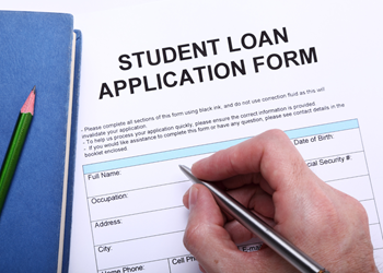 A hand holds a pen while filling out a student loan application form. 