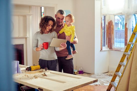 A family gathers around looking at a tablet in a room that is currently being remodeled.