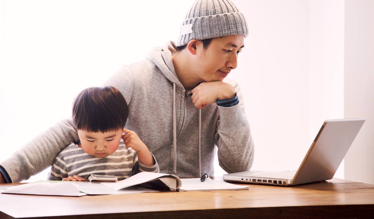 Man sits with his son while using a laptop.