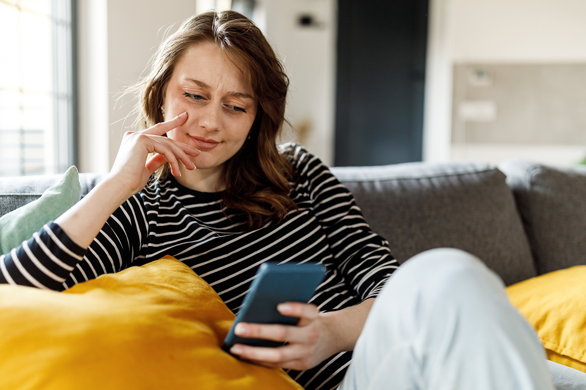 A woman sits on her couch and looks suspiciously at a smartphone screen