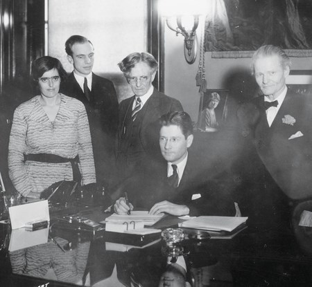 An old black and white image showing some of the original founders of UW Credit Union gathered behind a desk in an office. 