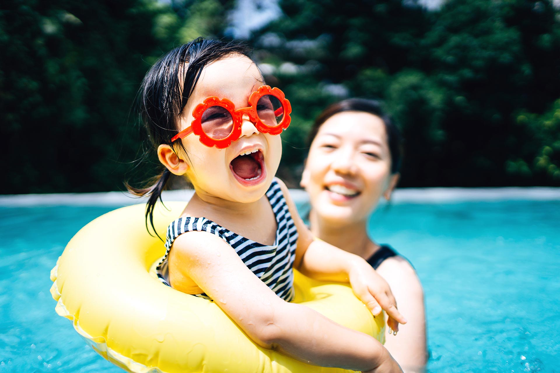 Mother and young daughter enjoying time in a pool while on vacation after learning how to vacation for less with UWCU.