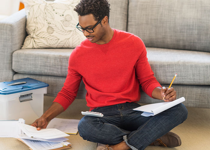 A man sits on the floor and works on his budget spreadsheet.