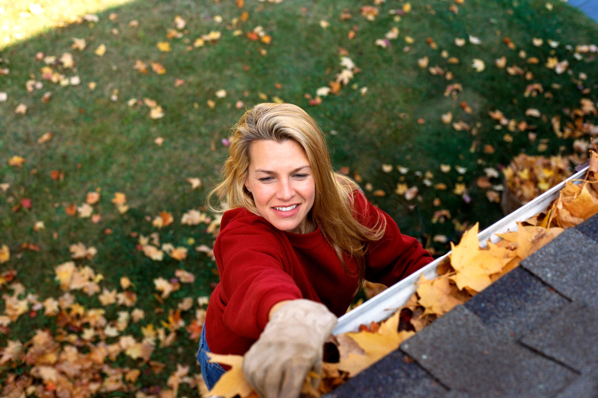 Woman cleans leaves out of a gutter to prepare her home for winter.