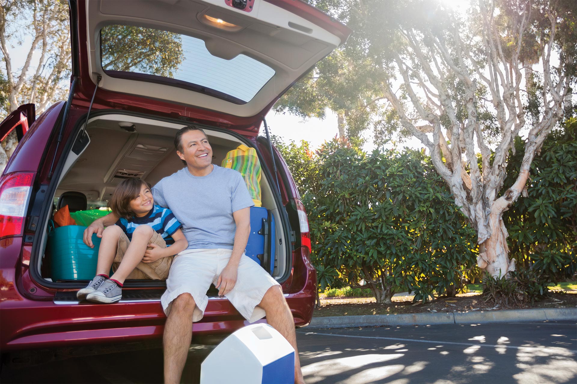 Father and son sit inside the open back end of their vehicle ready for a fun adventure.