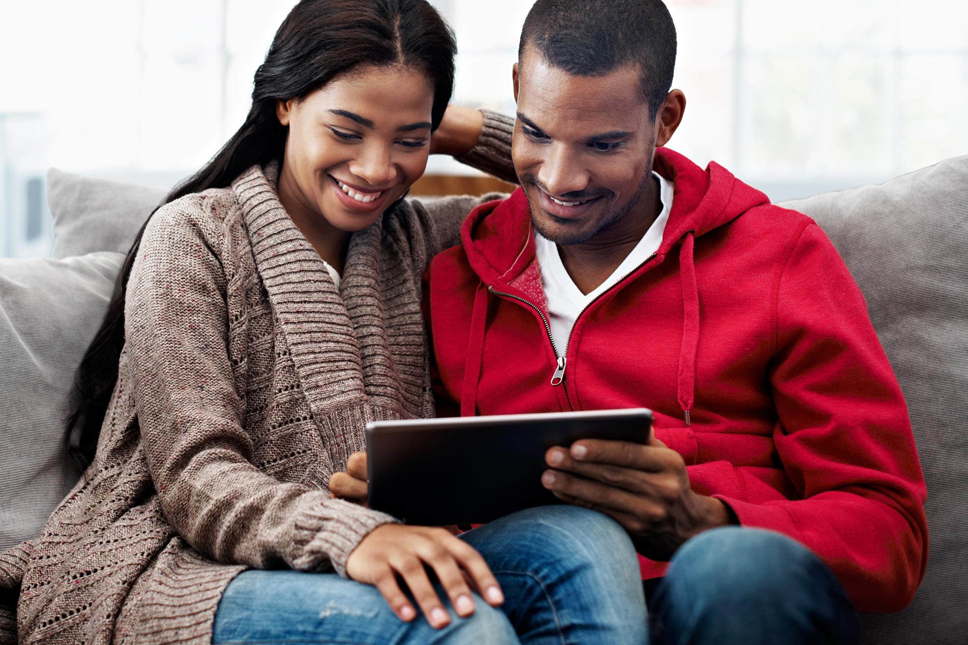 Couple sits on a couch looking at finances on a tablet.