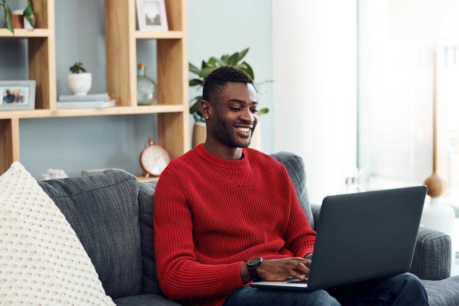 Young man sitting in his living room with his laptop checking is credit score on UWCU's Web Branch.